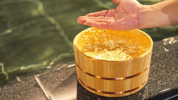 A hand pouring water into a wooden bowl on a granite countertop. - Natural Hot Spring SUPER HOTEL Kumamoto Chamber of Commerce (Kumamoto)