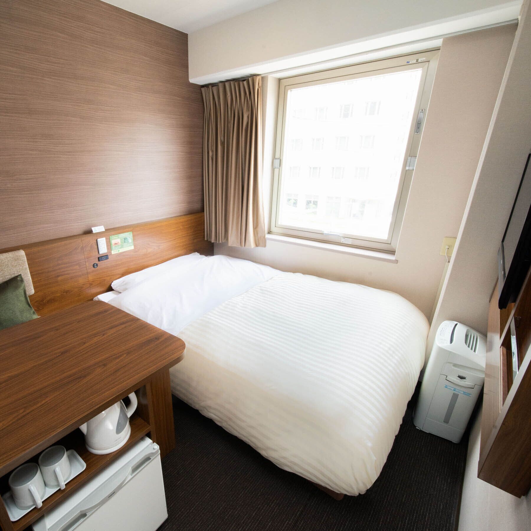 A hotel room with a wooden headboard, a single bed, a small table with a kettle, a TV, and a waste bin.