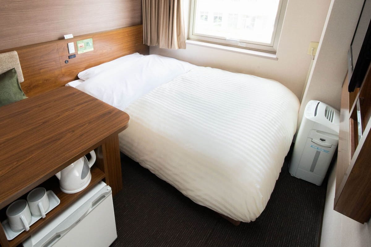 A hotel room with a wooden headboard, a single bed, a small table with a kettle, a TV, and a waste bin.