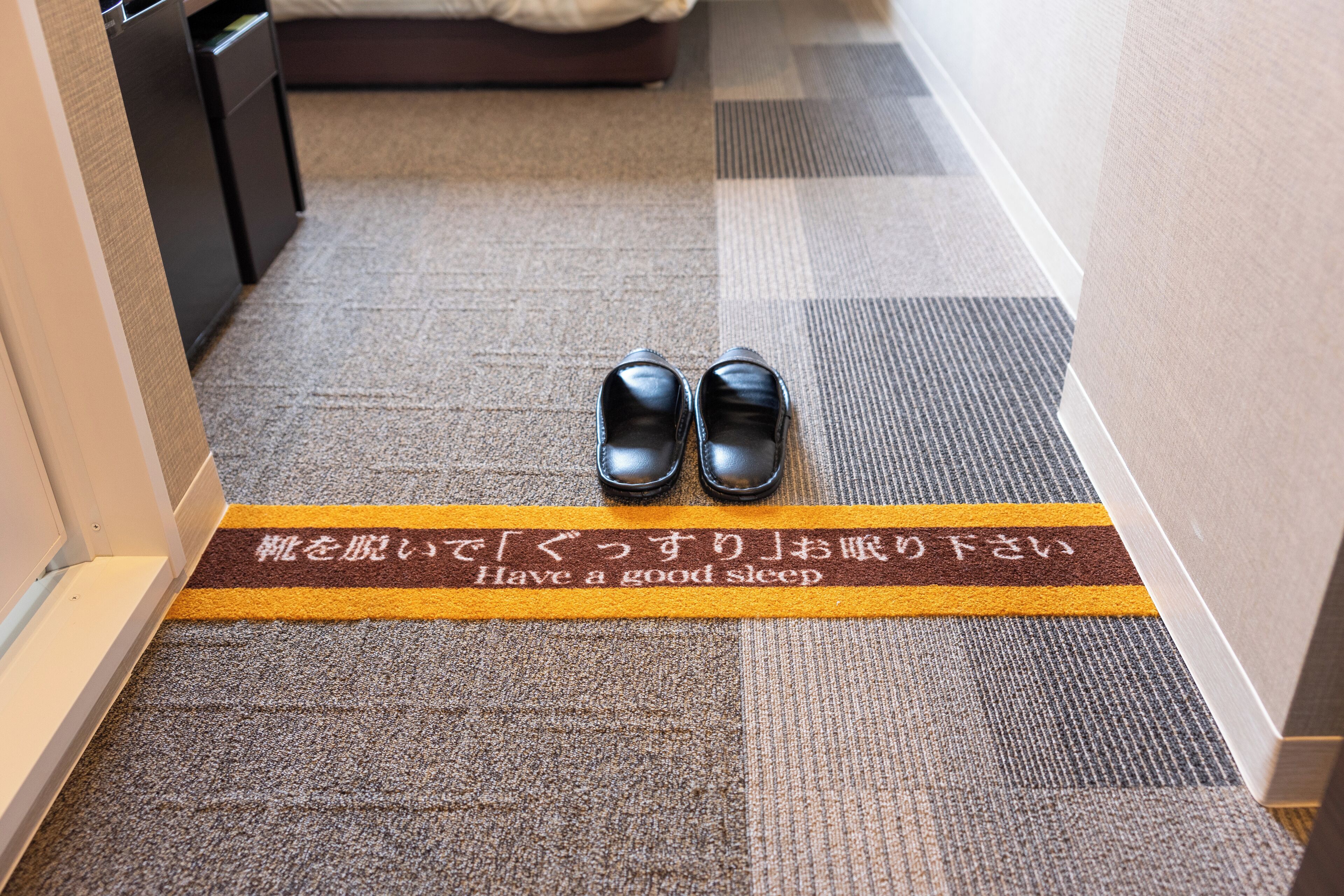 A carpeted hallway with a pair of shoes and a mat that says "Have a good sleep."