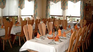 A dining area with wooden chairs and tables set for a meal, large windows with curtains, and a ceiling with a light fixture. - AdiHotels 'Haus Gombert' (Knullwald)