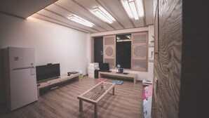 A compact kitchen with a refrigerator, a flat-screen TV, and a wooden table. - Wansangol Guesthouse (Jeonju)