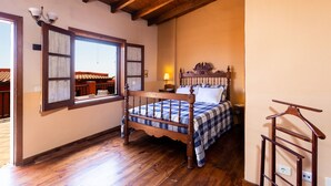 Un dormitorio con cama de madera, ventana con cortinas, mesita de noche y perchero.