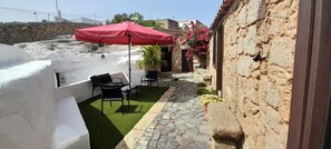 Eine Terrasse mit Steinboden, einem roten Sonnenschirm und Sitzgelegenheiten.