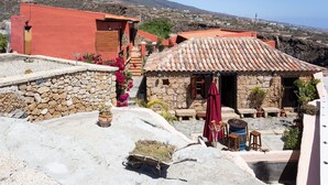 Un edificio de piedra tradicional con tejado de tejas, una pared de piedra y un pequeño jardín con macetas y flores.