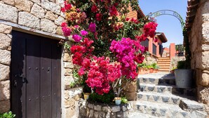 Un edificio de piedra con una puerta de madera oscura, una escalera de piedra y una jardinera con flores rosas.
