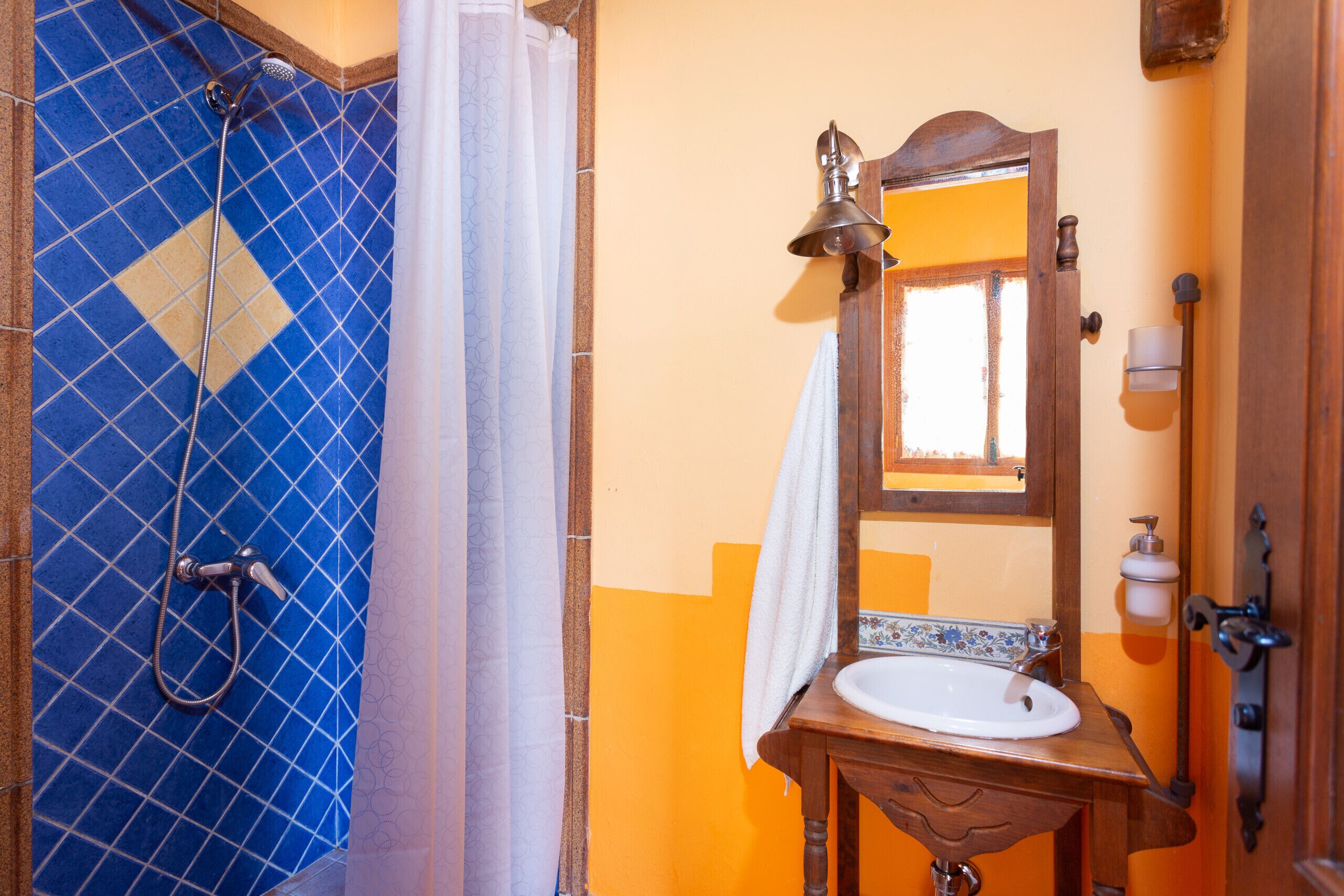 A bathroom with a blue-tiled shower, a wooden sink, and a mirror with a wooden frame.