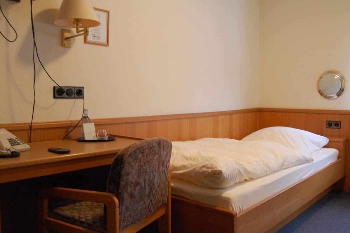 A hotel room with a single bed, a desk with a telephone and a lamp, and a chair.