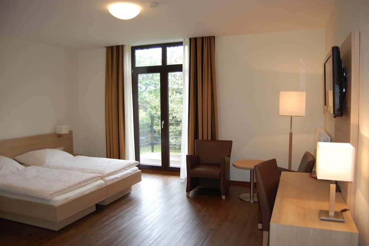 A hotel room with a bed, a chair, a small table, a lamp, and a TV.