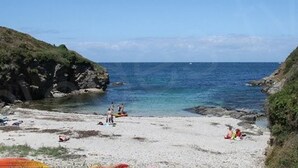 A beach with rocky cliffs, clear blue water, and people relaxing on the sand.