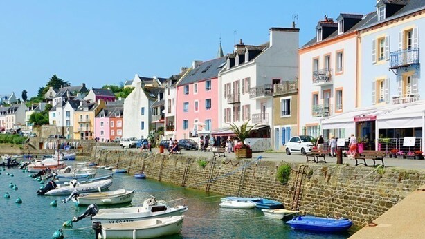 A coastal town with colorful buildings, a stone wall, and boats docked along the water.