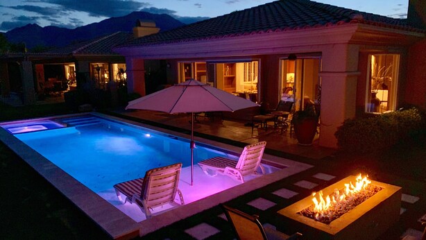 Ein Swimmingpool mit Liegestühlen und einem Feuerkorb, umgeben von einer Terrassenfläche mit Blick auf Berge im Hintergrund.