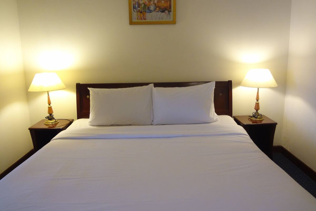 A neatly made bed with white linens and two bedside lamps on wooden nightstands.