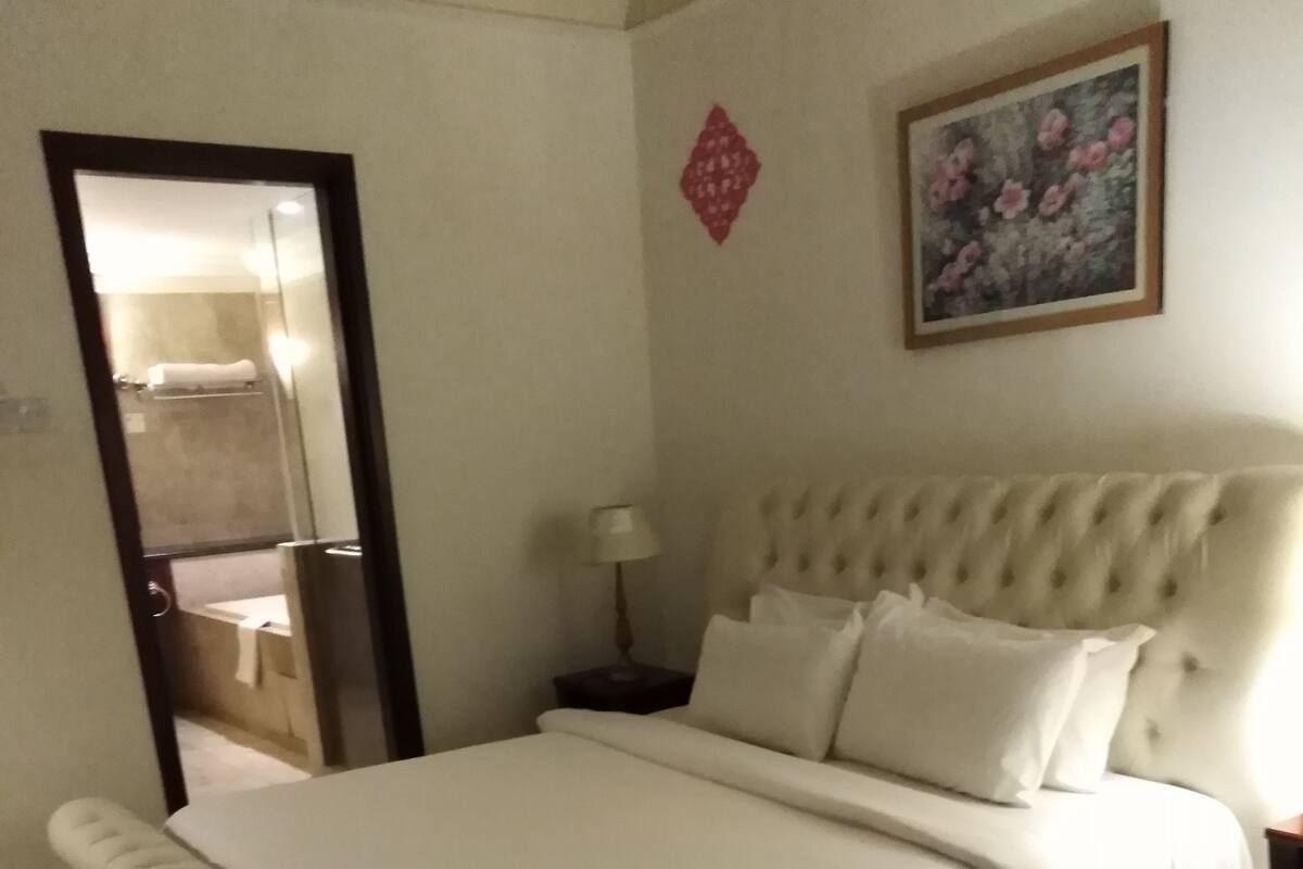 A hotel room with a large bed, a nightstand with a lamp, a mirror, and a painting on the wall.