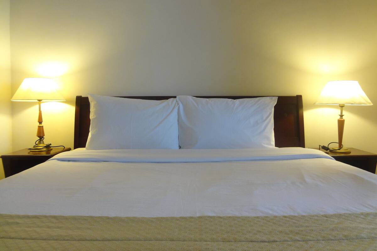 A neatly made bed with white linens, two bedside lamps, and a wooden headboard.
