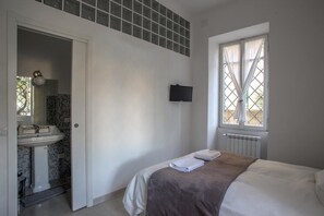 A bedroom with a bed, a window, a TV mounted on the wall, and a bathroom visible through an open door. - Equilibrì Guest House (Rome)