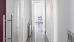 A narrow, well-lit hallway with white walls and a tiled floor, leading to a room with a table and chairs. - Equilibrì Guest House (Rome)