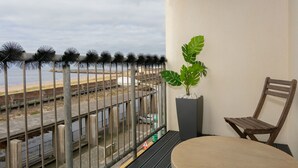 A balcony with a view of the beach, a potted plant, and a wooden chair. - Harris Retreat - Donnini Apartments (Ayr)