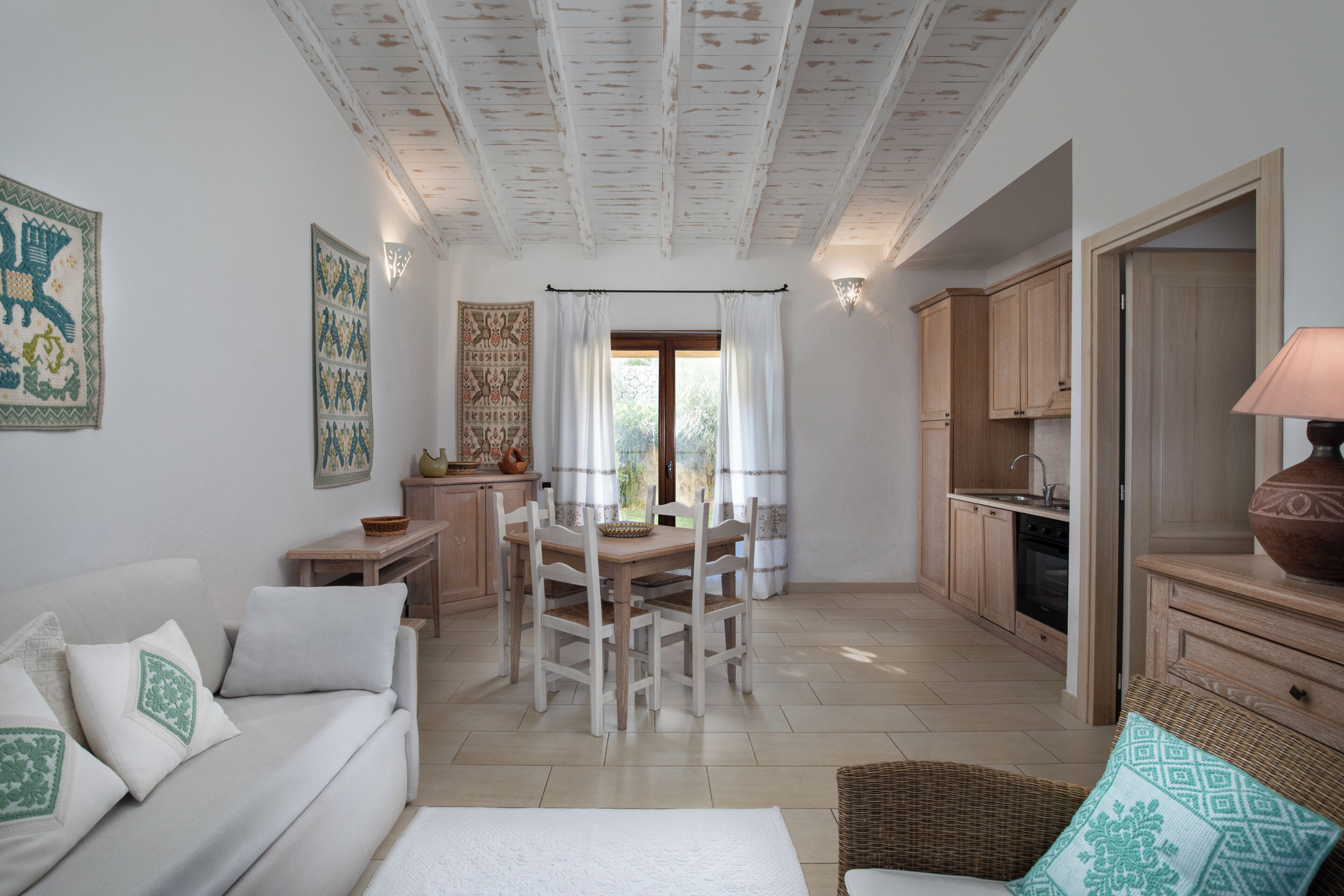 A room with a dining table, chairs, a sofa, a kitchen area, and a large vase.