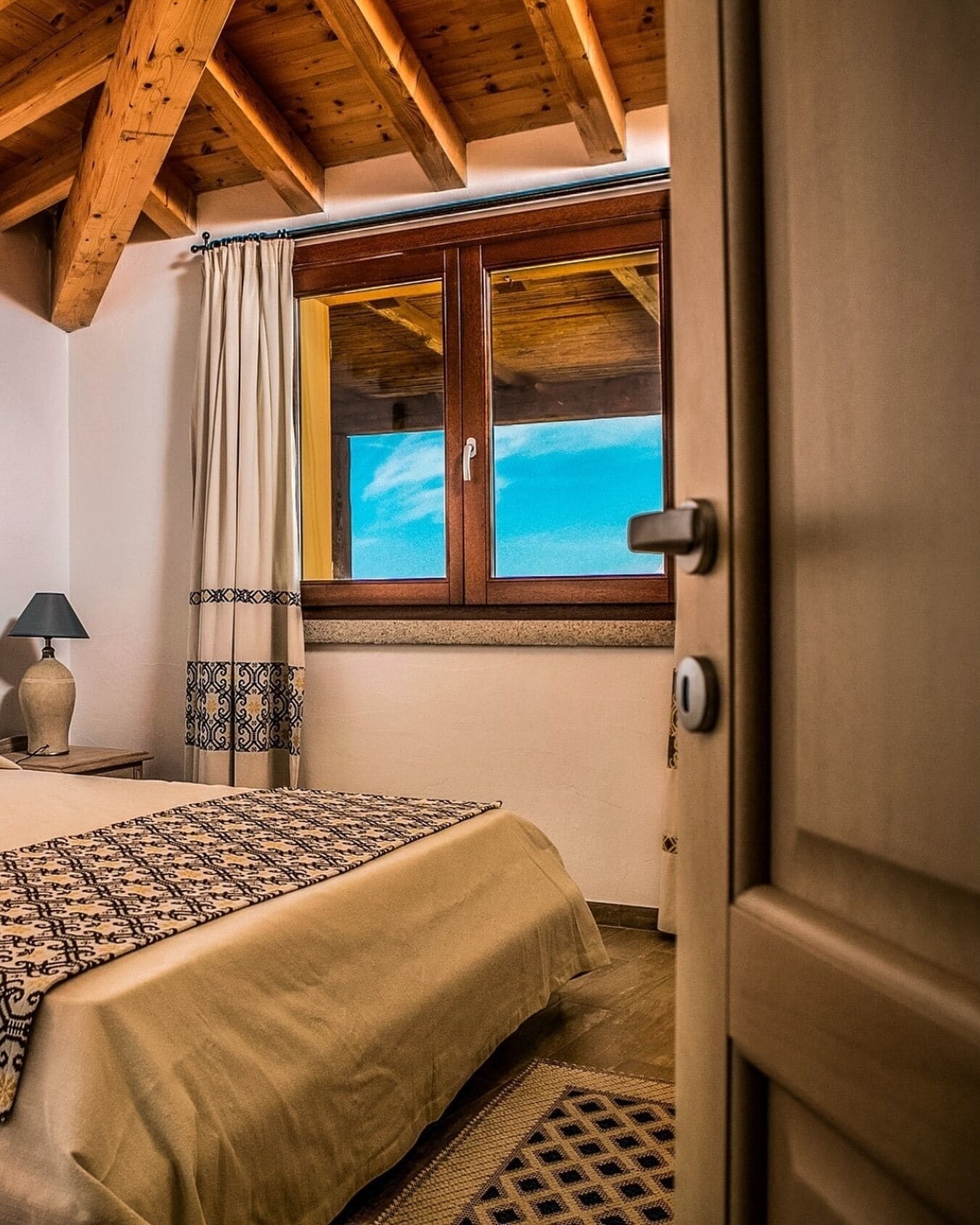 Un dormitori amb un llit, una finestra amb vista, una porta i una làmpada.