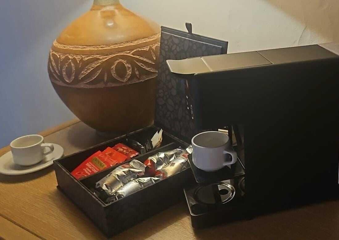 Una mesa con una taza de café, un termo, una caja de bolsitas de té y un jarrón decorativo.