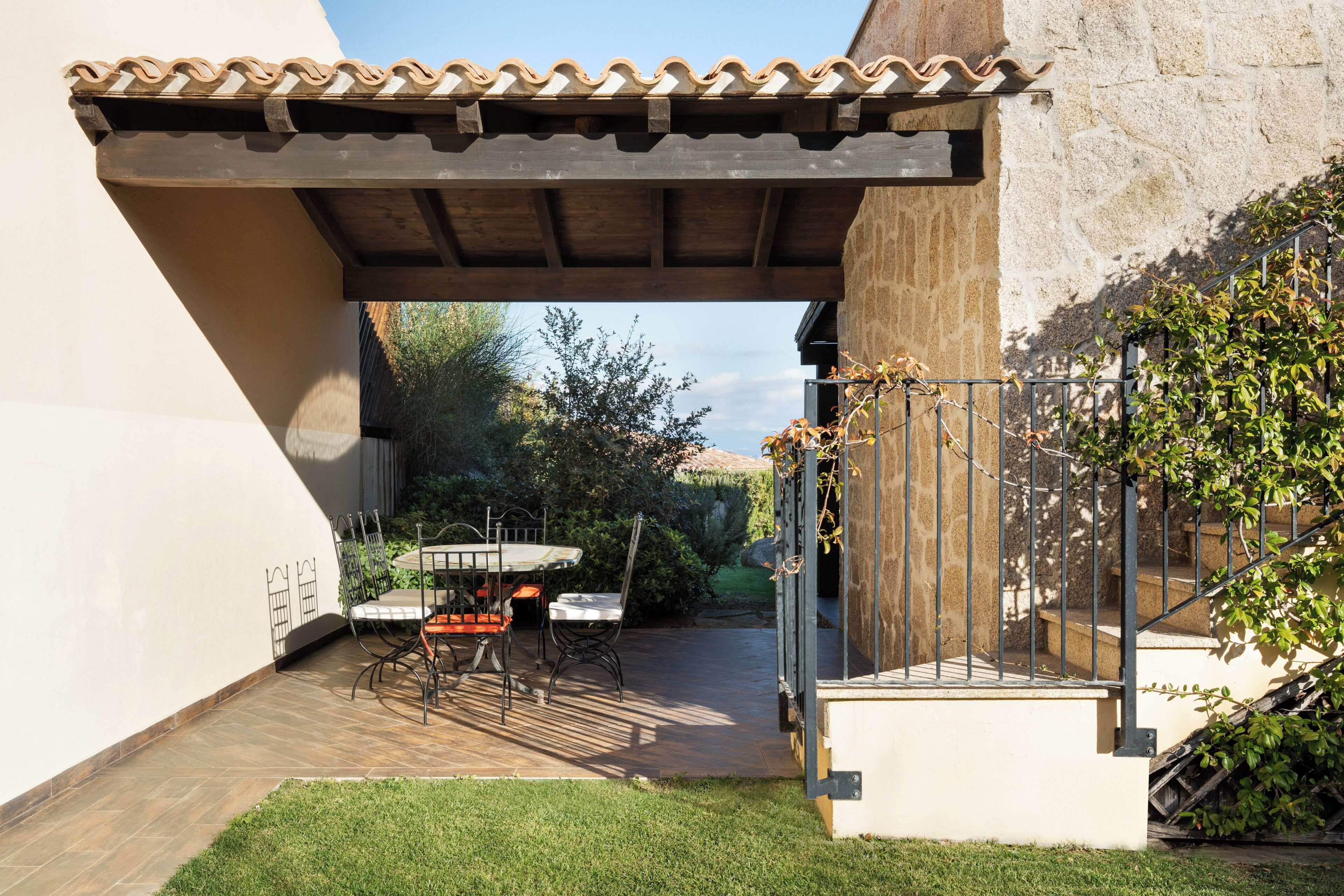 Un patio al aire libre con una mesa, sillas, una pérgola y una escalera que lleva a un edificio de piedra.