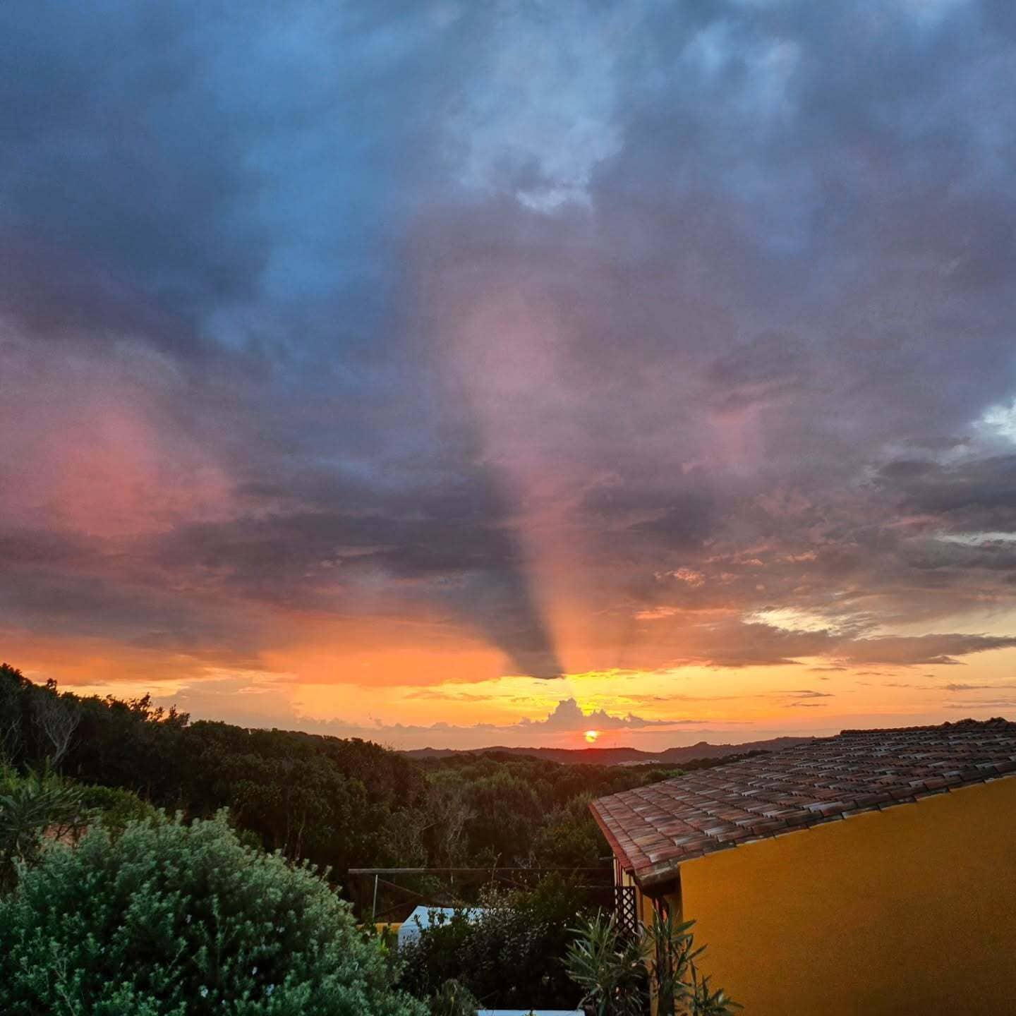 Solnedgang over et kuperet landskab med en bygning i forgrunden.