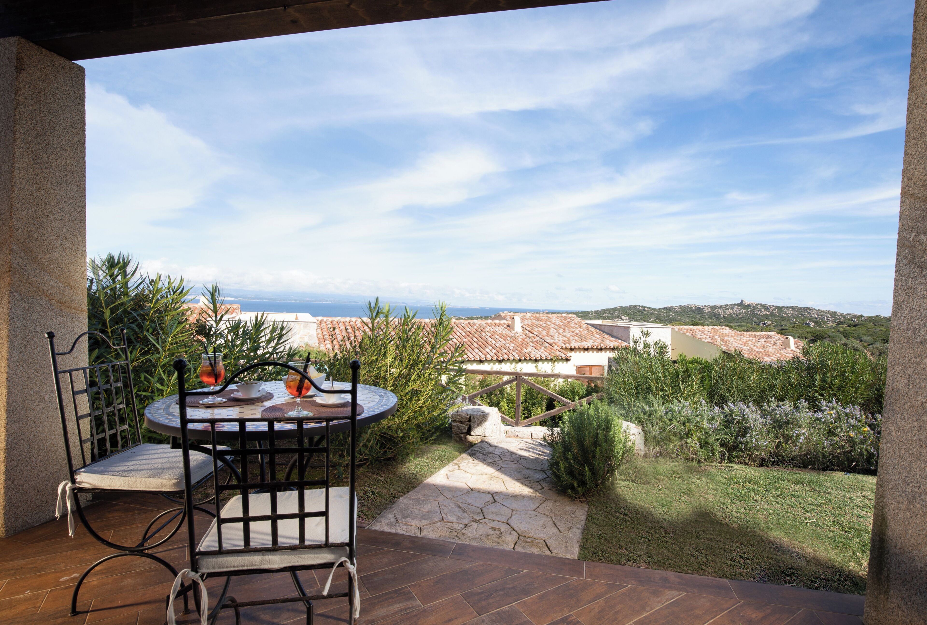 A patio with a table and chairs, overlooking a scenic view of the sea and terracotta-roofed buildings.