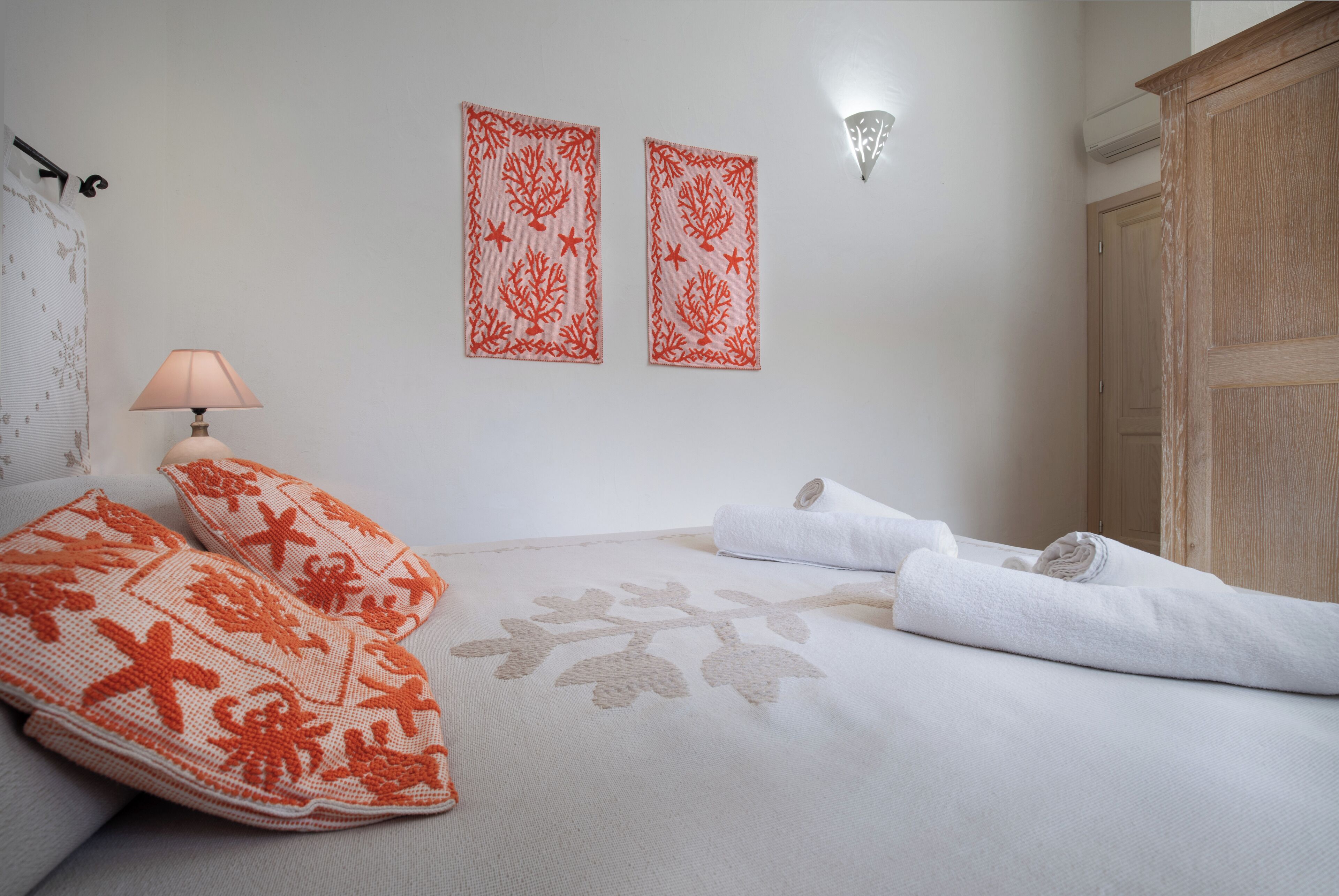 Une chambre à coucher avec un lit, des oreillers, une lampe, un luminaire fixé au mur et une porte.
