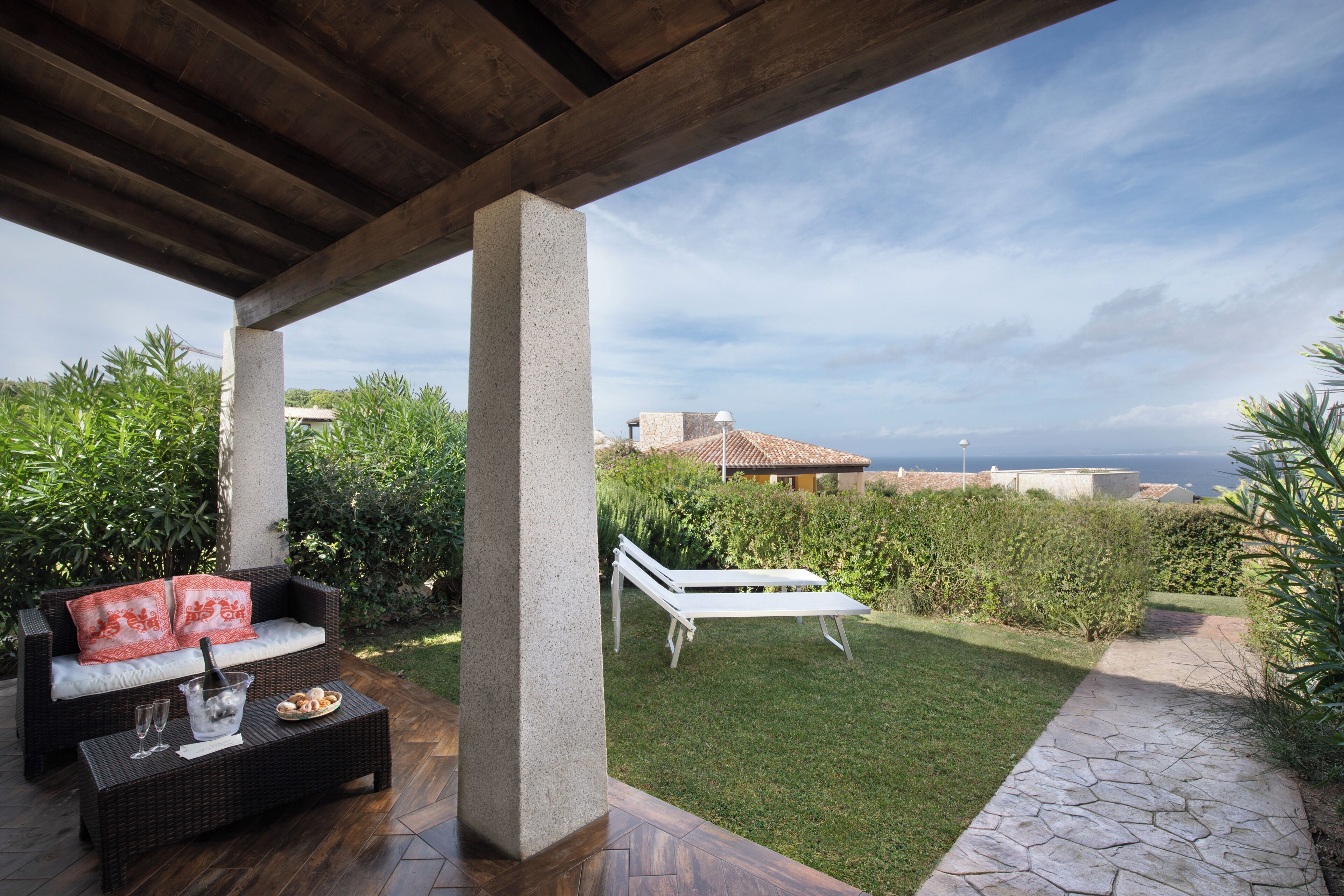 Un espace extérieur aménagé, abrité et doté d'un canapé en osier et d'un fauteuil de relaxation, d'un chemin en pierre et d'une vue sur la mer.