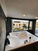 A modern bathroom with a large bathtub, a window with curtains, and a view of a residential area.