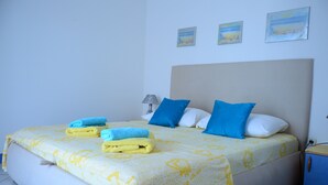 Een net opgemaakt bed met blauwe en witte kussens, een lamp en een klein nachtkastje.