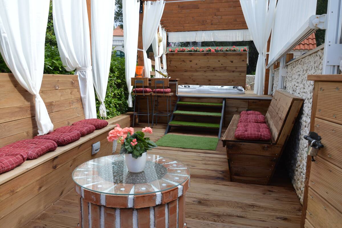 A cozy outdoor seating area with a round table, cushioned benches, and a small garden.