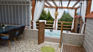 Een terras met een stenen vloer, een houten tafel met stoelen, een groene mat en een jacuzzi.
