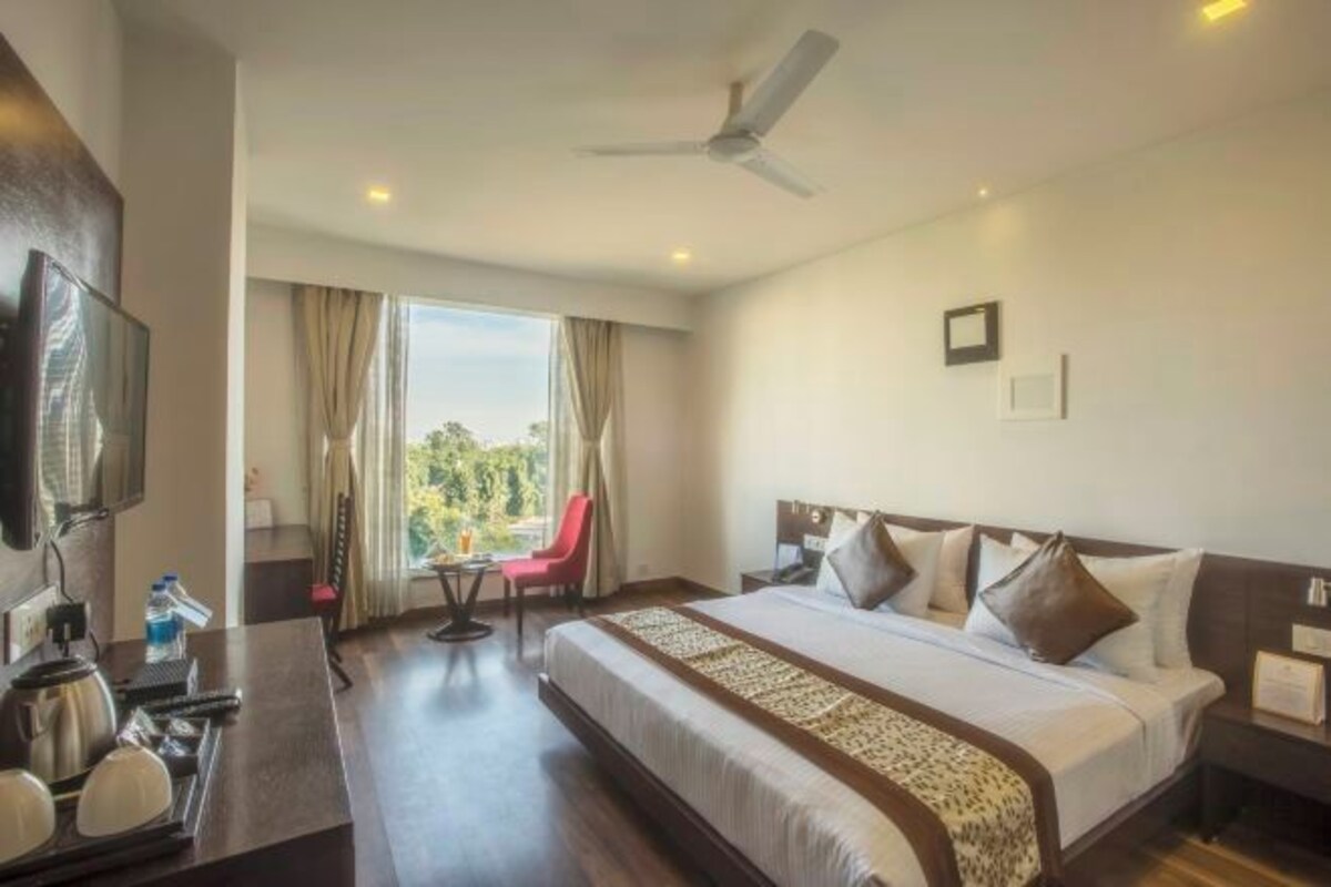 Habitación de hotel con una cama grande, un escritorio con hervidor, una silla y un televisor.