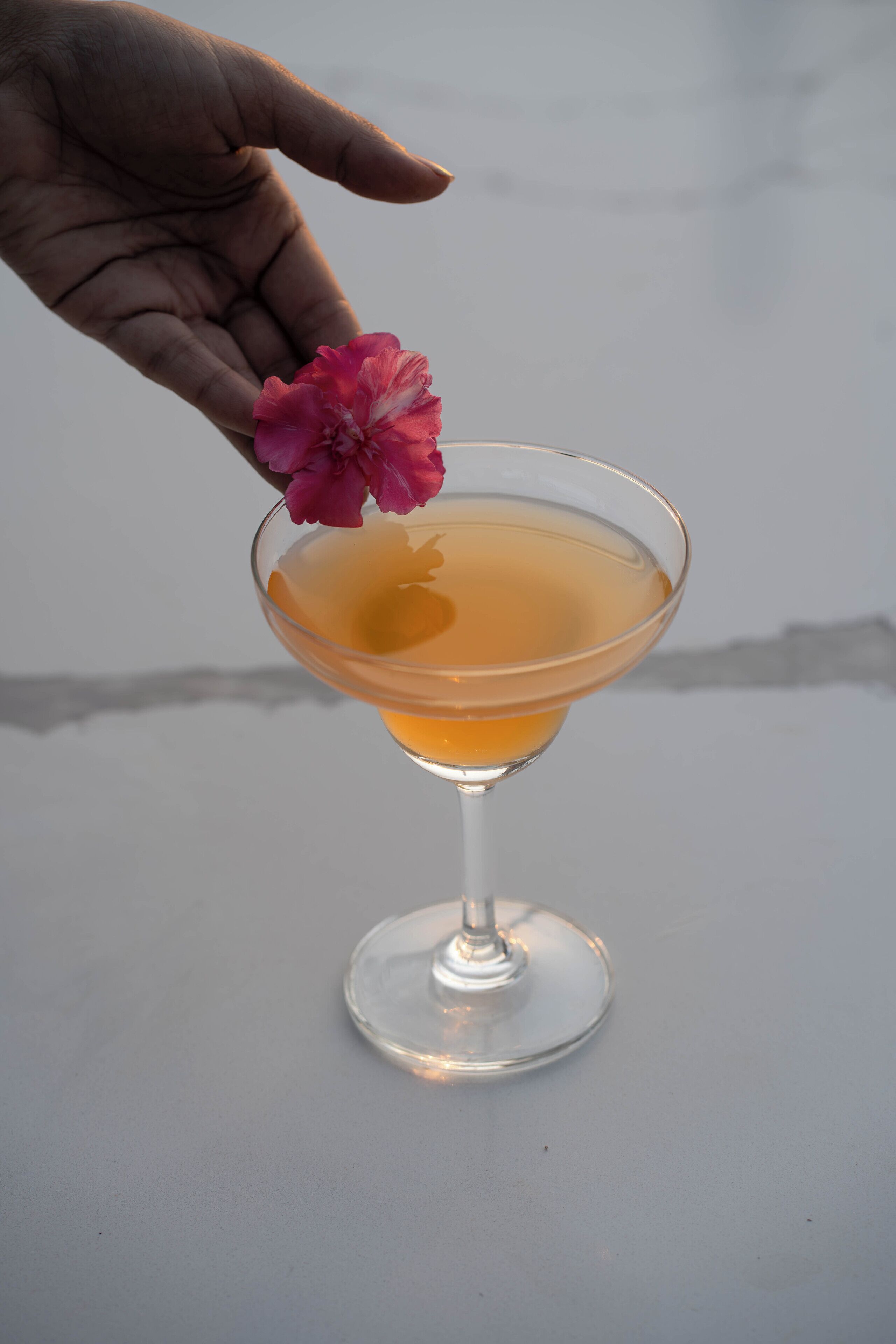 A cocktail glass with a pink flower on the rim, placed on a flat surface.