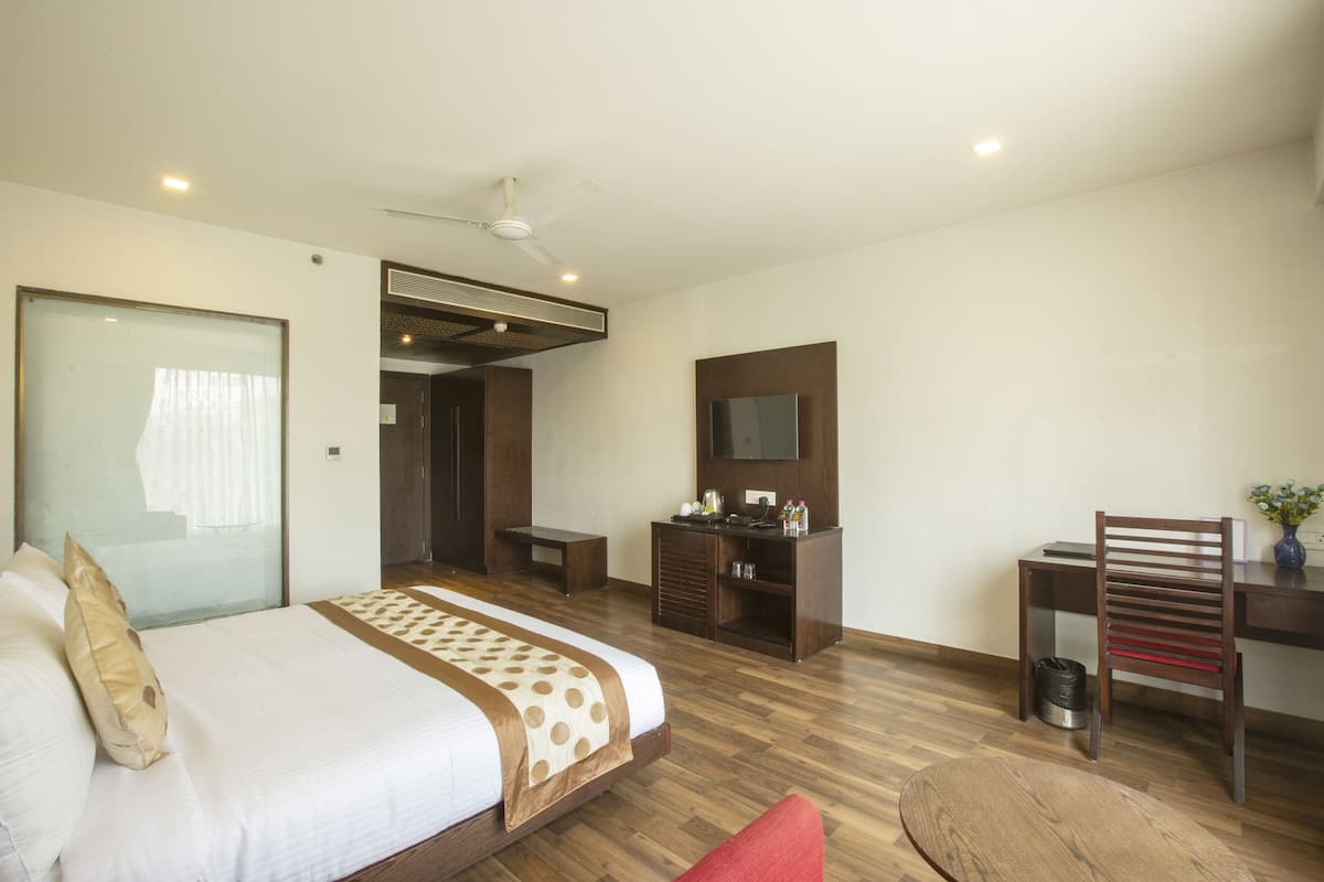 Een hotelkamer met een groot bed, een bureau, een stoel, een televisie en een plafondventilator.