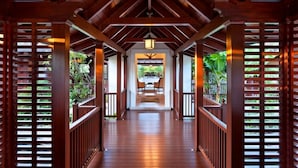 A wooden covered walkway with a central table and chairs, flanked by wooden railings and greenery. - Villa Alila (Holetown)