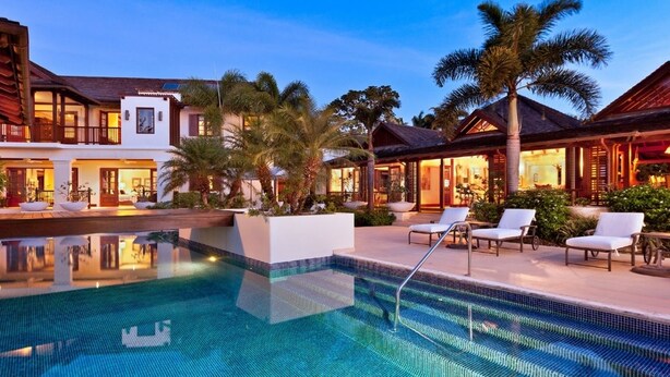 A pool area with a clear blue pool, lounge chairs, and a well-lit building with multiple windows and balconies. - Villa Alila (Holetown)