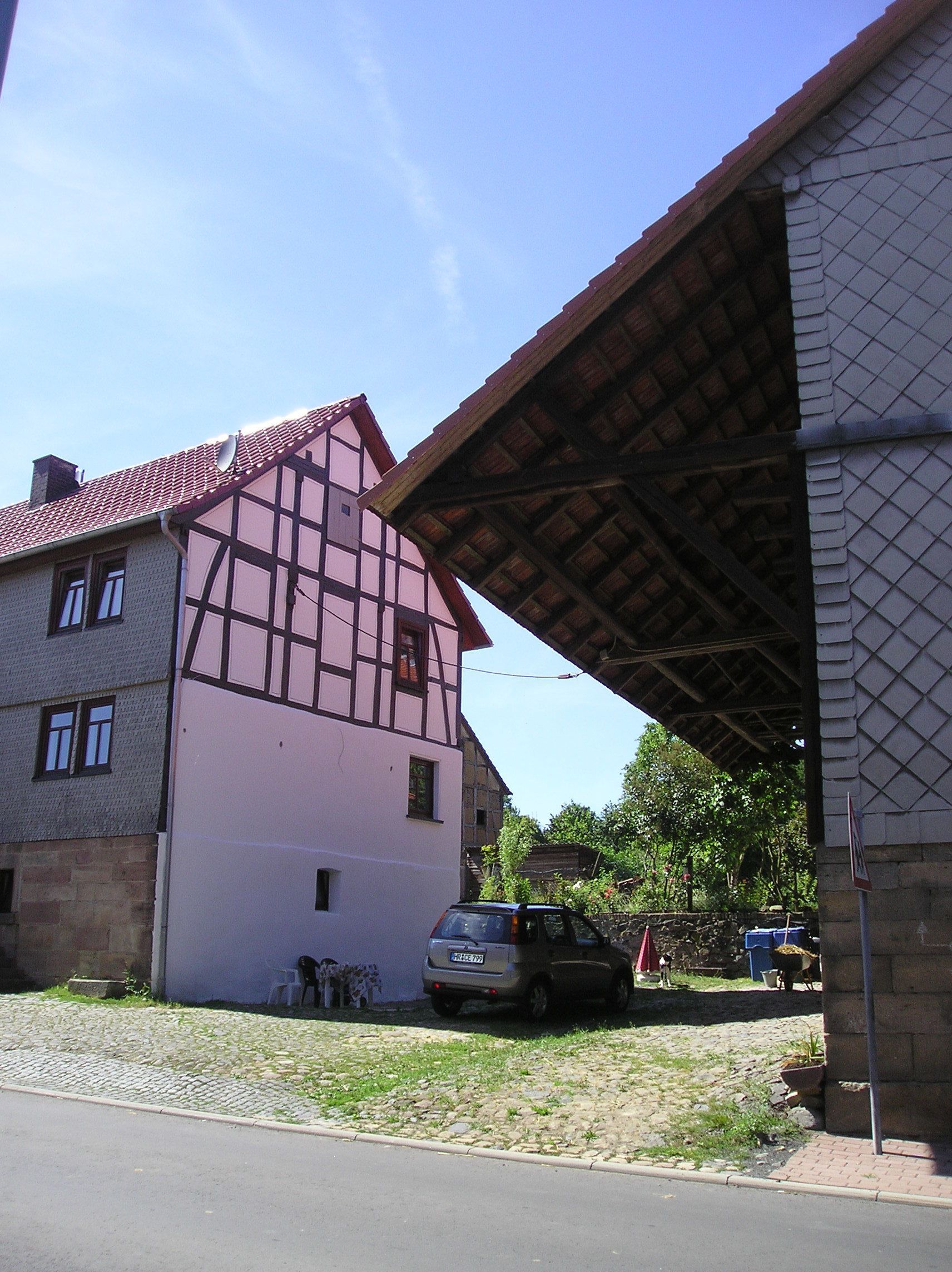 A traditional half-timbered house with a sloped roof, a parked car, and a cobblestone driveway.