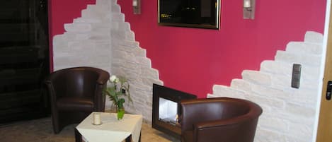 A room with a fireplace, two leather chairs, a small table with a candle and a vase, and a red wall.