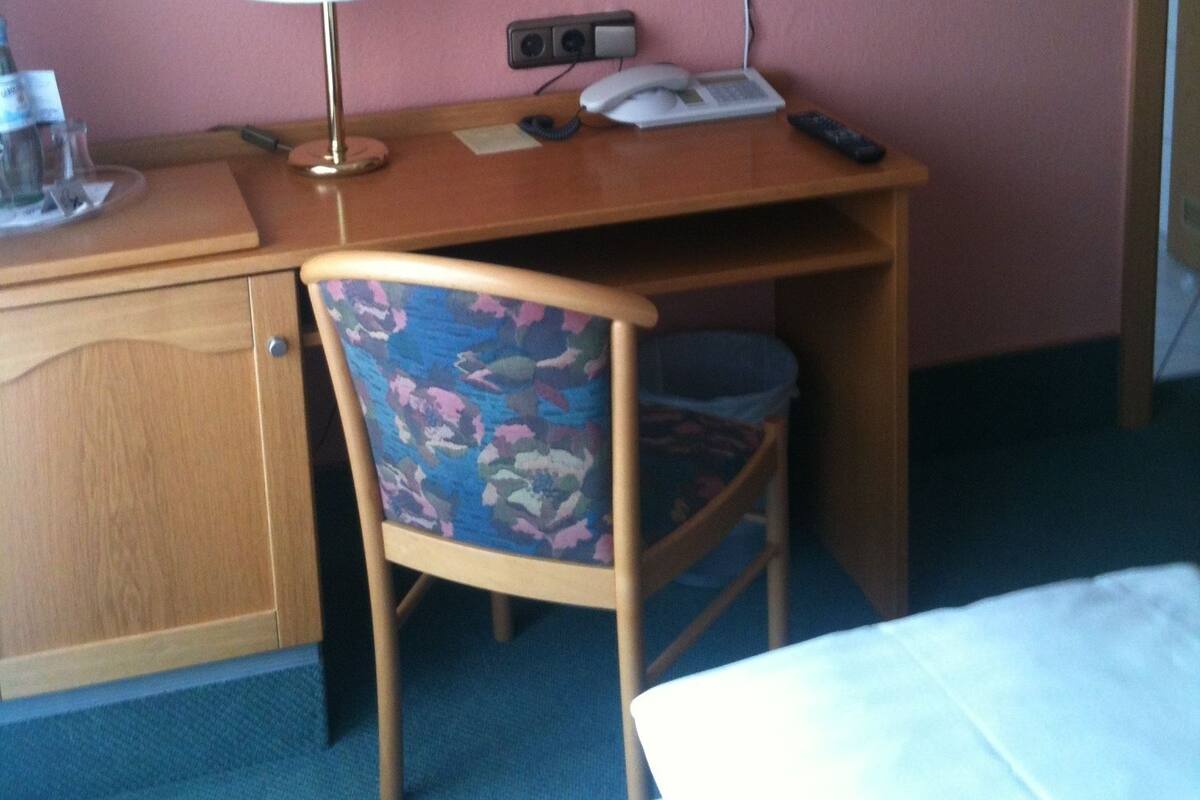 Una habitación de hotel con un escritorio de madera, una silla, un televisor montado en la pared y una lámpara.