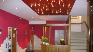 A lobby with a red wall, a wooden reception desk, a staircase, and a reception area with a red carpet. - Knüllhotel Tann-Eck (Knullwald)