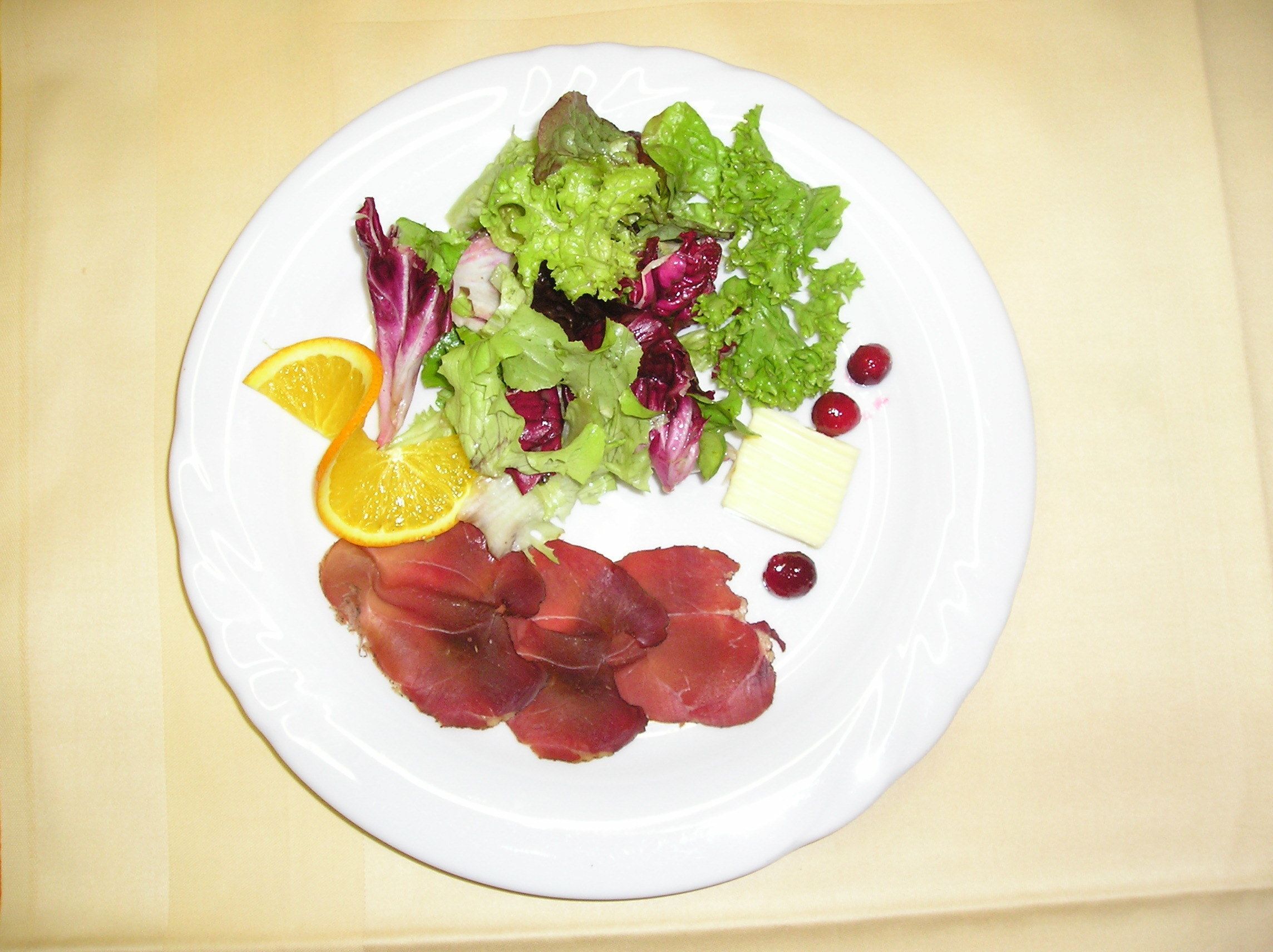 A plate with a variety of food items including greens, meat, cheese, and citrus.