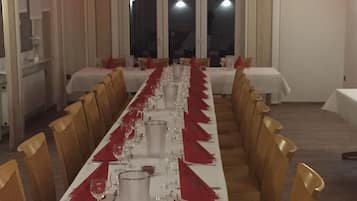 Een lange eettafel gedekt met rode servetten, glazen en bestek, omringd door houten stoelen.