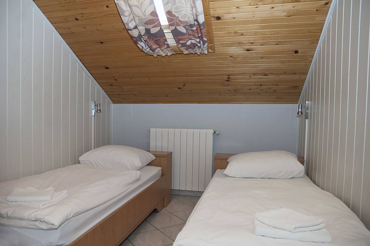 Una habitación pequeña y luminosa con dos camas individuales, techo de madera y un radiador.