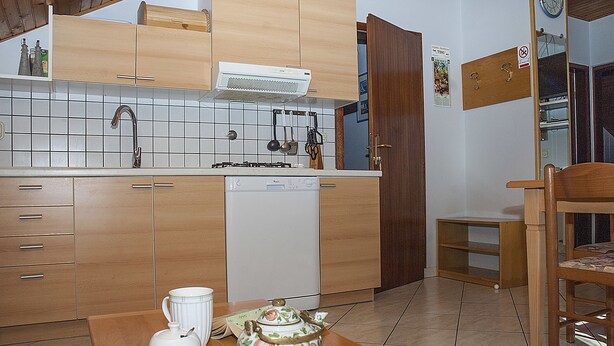 A compact kitchen with wooden cabinets, a dishwasher, and a dining table with a teapot and cup. - Villa Paolija (Novigrad)