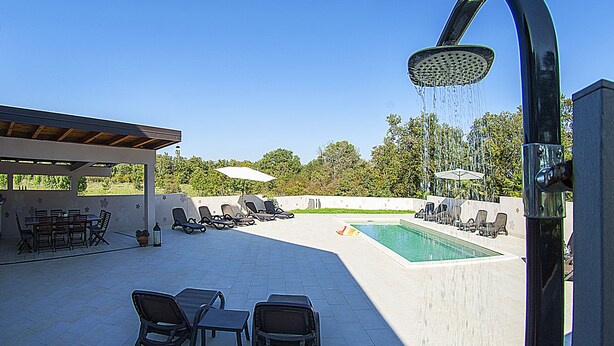 Una zona junto a la piscina con ducha integrada, sillas de descanso y un área de estar cubierta.