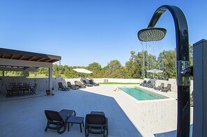 Un espace aménagé au bord de la piscine, comprenant une douche intégrée, des chaises longues et un coin salon abrité.