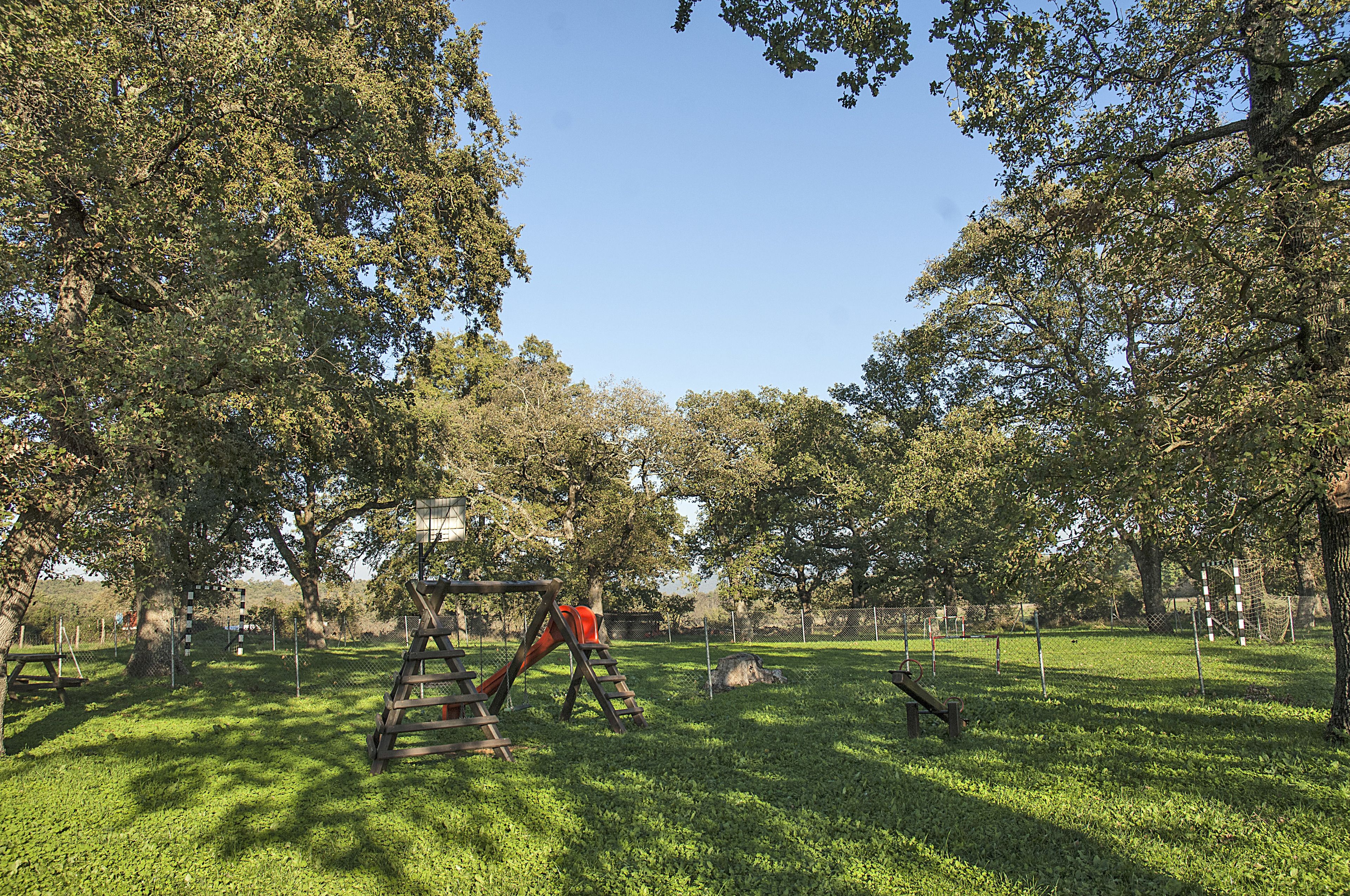 Un parque con un área de juegos, árboles y un campo cubierto de césped.